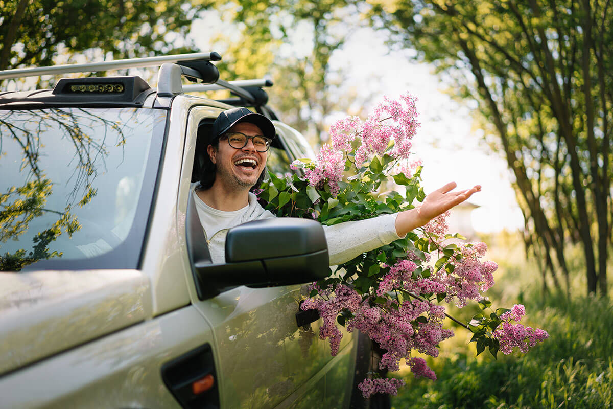 Happy man driving car with lilac in forest