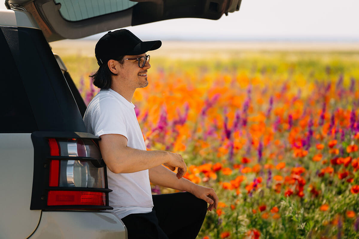 Man sitting in car trunk by colorful meadow