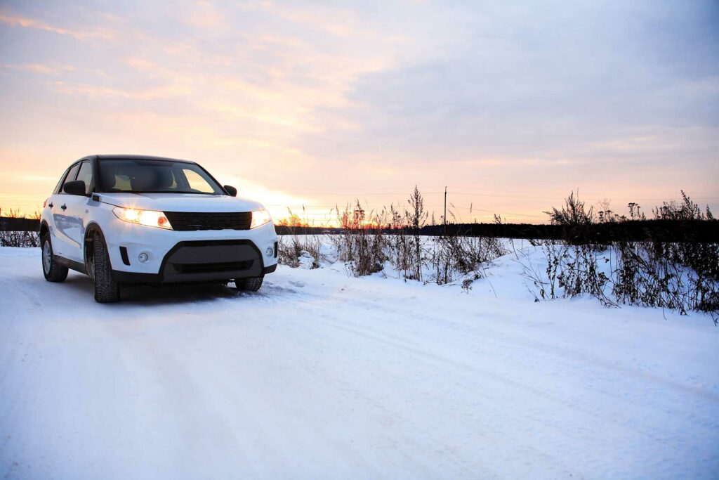 SUV driving on a snowy road with a sunset in the background